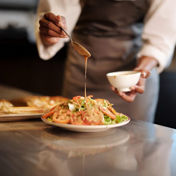Restaurant cook pouring dressing over fresh delicious salad